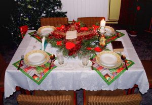 Mesa de Natal posta com toalha branca, pratos, velas e centro de mesa vermelho