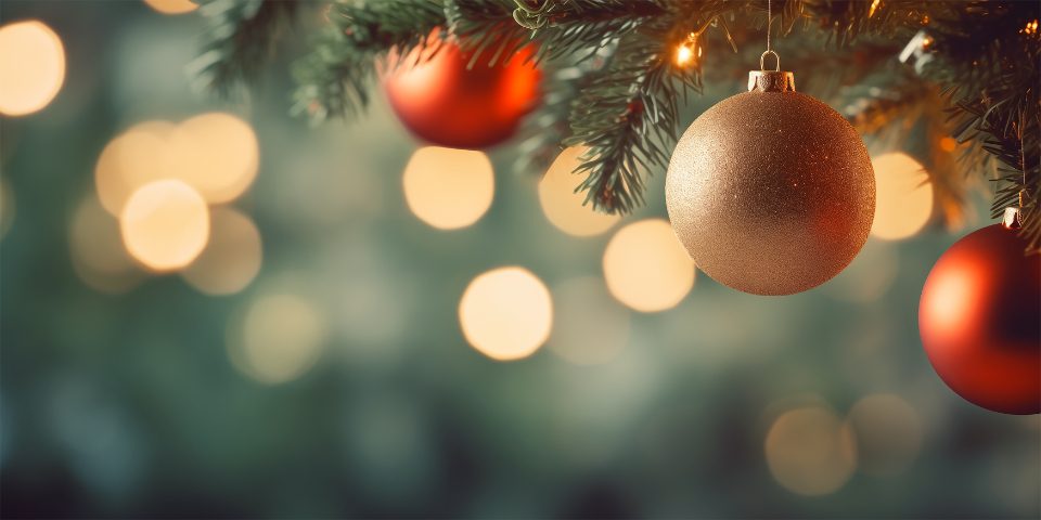 Bolas de Natal vermelhas e douradas penduradas na árvore com luzes ao fundo