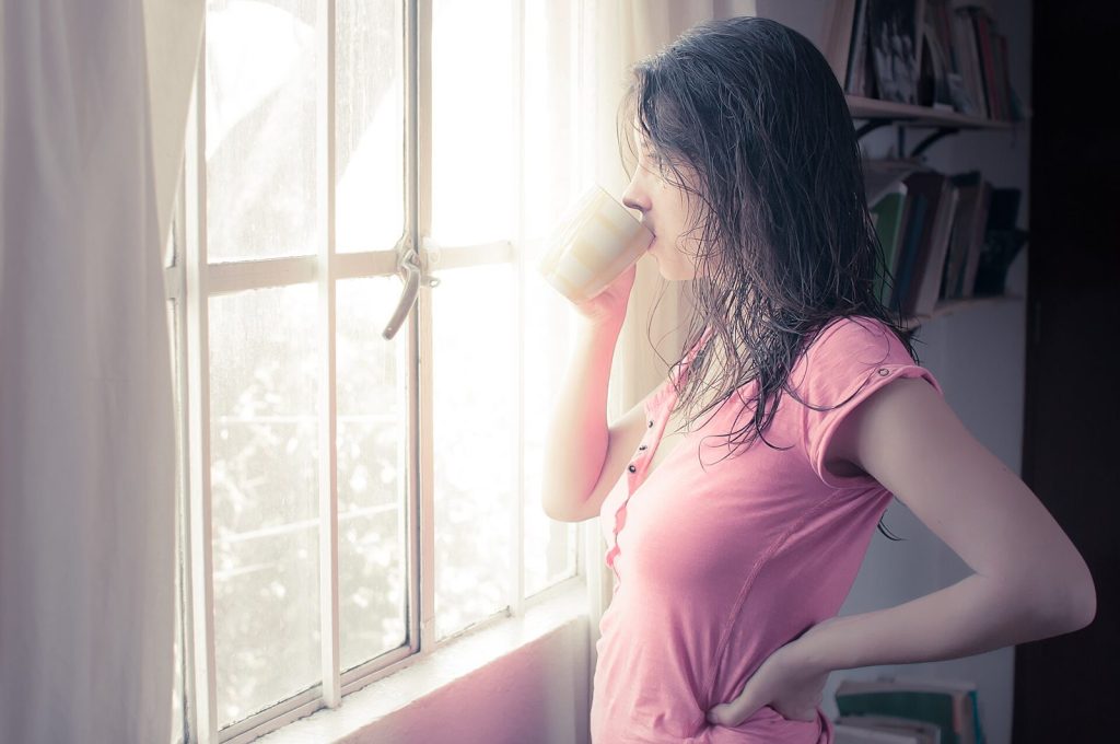 Mulher tomando café perto da janela pela manhã